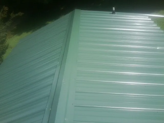 New green metal panels meeting at the ridge of a roof — Flat Roof Repair work by our crew in Richwood