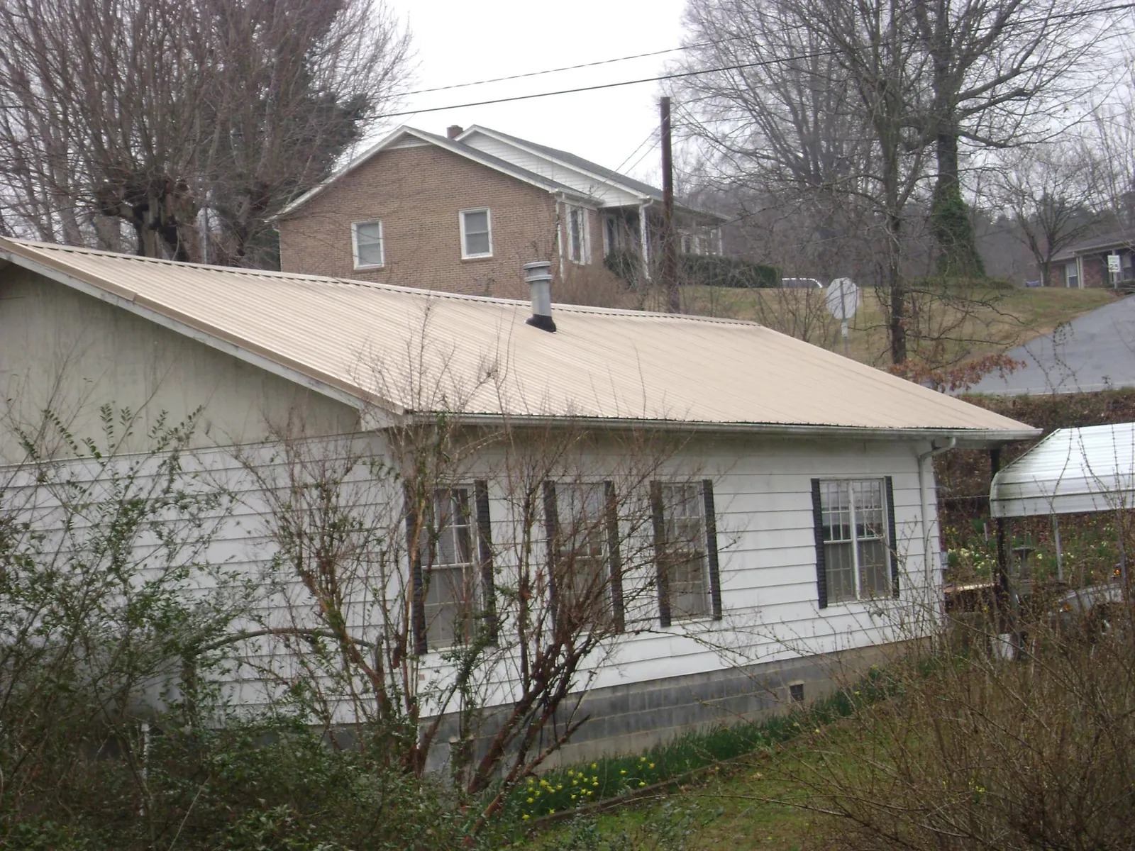 Tan metal roof on a white sided house set into a hillside — Commercial Roofing by Roofing Brothers in Richwood