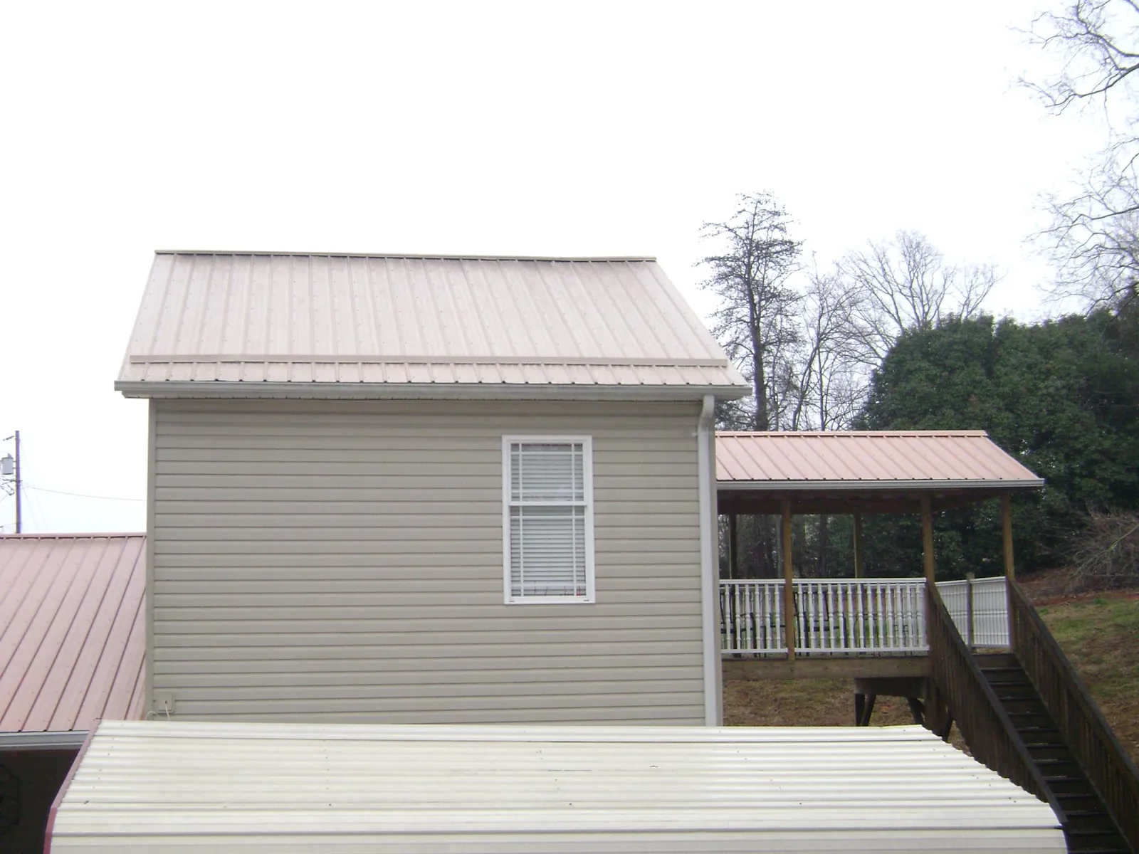 Tan metal roofs on a two story addition and attached porch, from a Roof Replacement job in Richwood